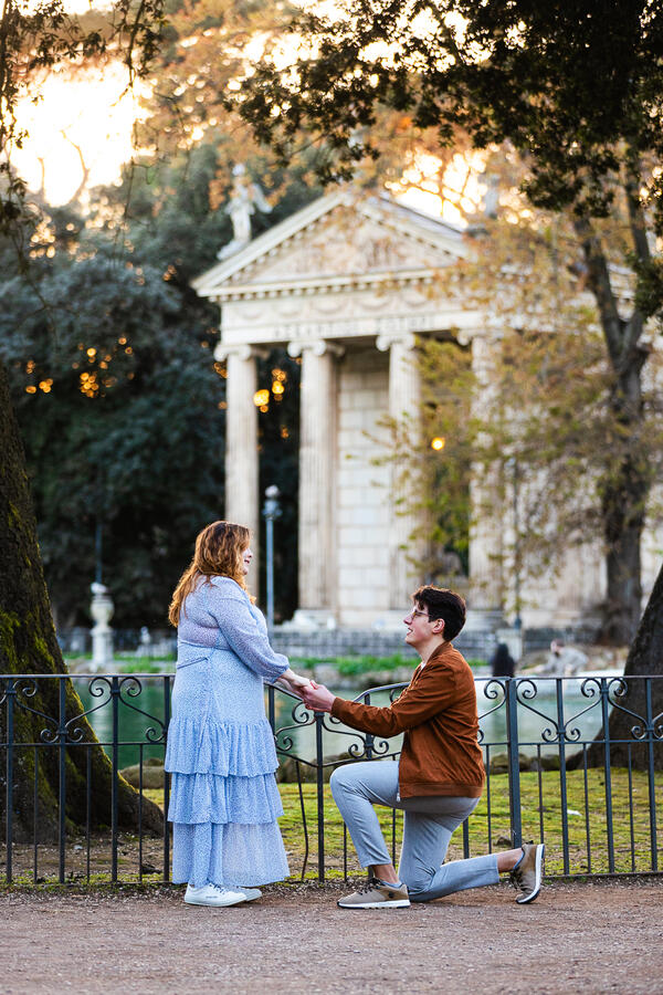 Guy proposing in Villa Borghese by the pond with the Aesculapius Temple in the background