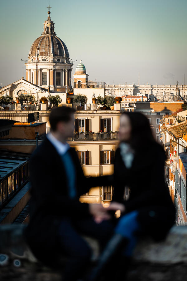 Newly-engaged couple in the foreground and out of focus, with Rome at sunrise in the background