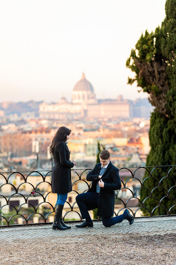 Young couple during their surprise wedding proposal on the Terrazza Belvedere at sunrise with the Vatican in the background