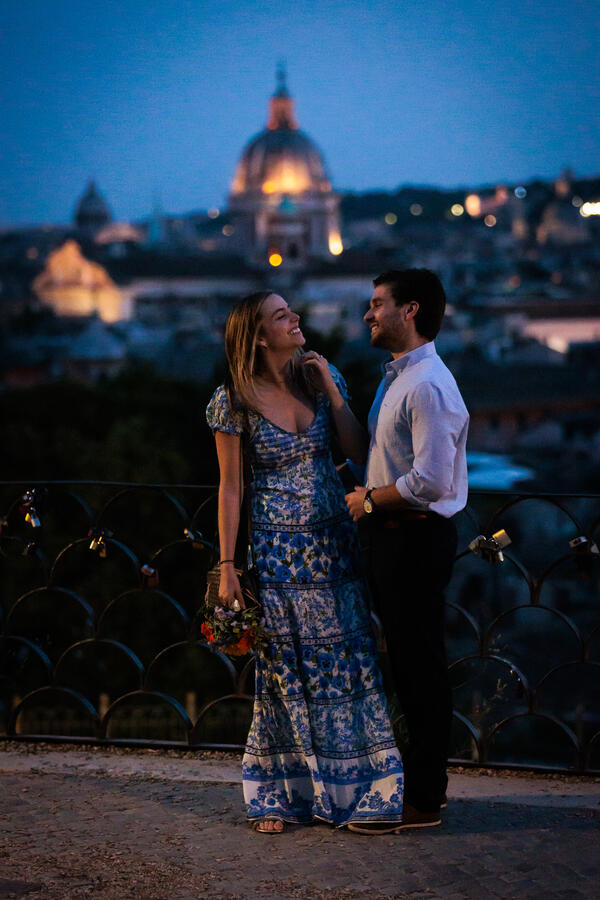 Happy couple smiling at each other during their surprise proposal on the Terrazza Belvedere at dusk in Rome